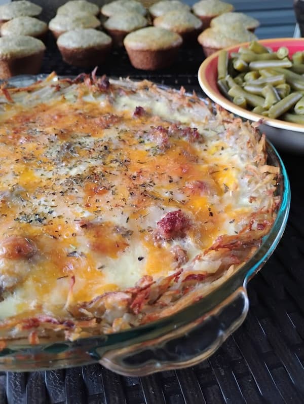 Close-up of a baked meat quiche with a crispy shredded potato crust, topped with melted cheese and herbs.