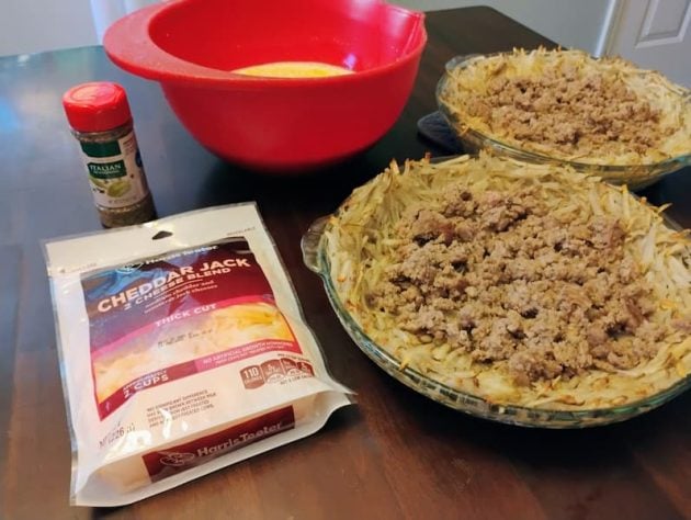 Two potato crusts in glass pie dishes partially filled with cooked ground sausage.