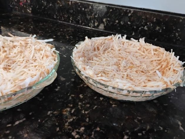 Two glass pie dishes filled with raw shredded potatoes pressed into the shape of crusts, sitting on a dark granite countertop as the base for a potato crust quiche.