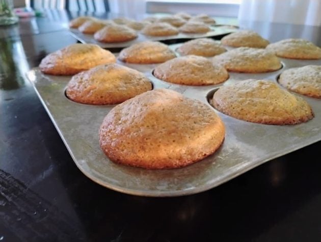 Freshly baked flax muffins cooling in metal muffin tins on a dark table.