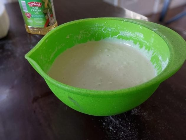 A bright green mixing bowl filled with easy 5-minute cornbread batter sits on a dark kitchen counter.