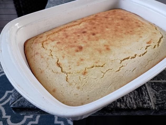 A freshly baked pan of golden cornbread sits in a white ceramic baking dish on a dark countertop.